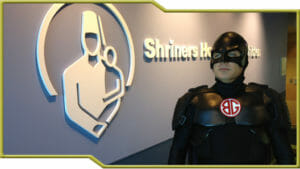 Sage dressed as a superhero posing in front of Shriners Hospital sign